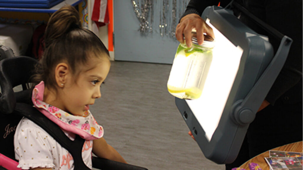 Image of a child looking at jar of liquid being held in front of a light box by a teacher